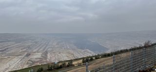 "Closer look into the mine Hambach. Some giant exvacators are at work in pits up to some hundred meters deep. Everything is brown and black. The sky is dark and cloudy and fog obscures part of the view."
