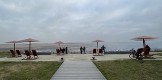"View into the coal mine Hambach. A footbridge leads to some metal chairs and parasols. In the background the cast nothingness of the mine reveals itself."