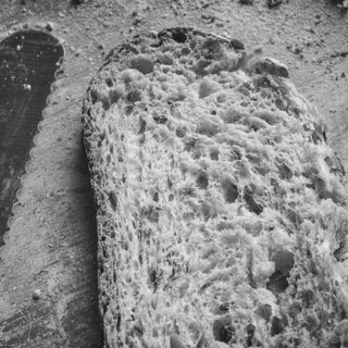 A slice of white bread, a bread knife and some breadcrumbs on a table