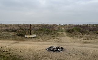 "The edge of the mine directly behind the forest. You see roughly 50 meters of earth until it suddenly disappears. A muddy service road is leads along the edge, someone lit a small fire on it."