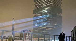 "The Amazon Tower in Berlin by night. A powerful projector projects «The wrong Amazon is burning» on its side."