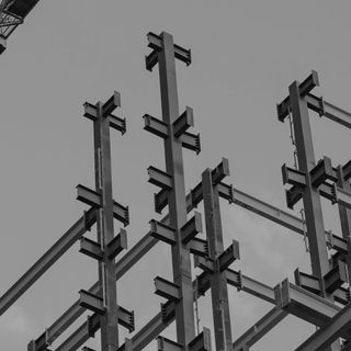 View of a construction site. There are steel beams visible, just the raw sceleton, against a slightly clouded but otherwise empty sky.