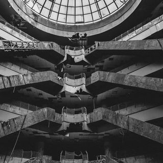 View of an old, decaying building. Probably an old shopping center, you can see escalators. Above all is a glass dome